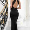 Brunette lady standing on staircase with open back black satin maxi dress.